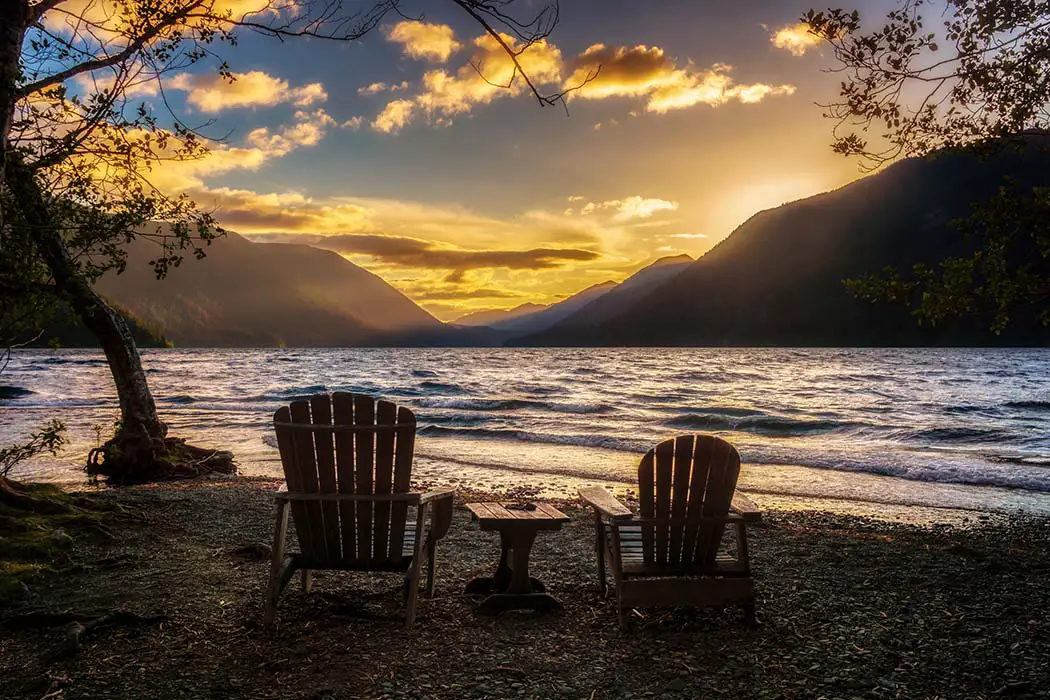 Sunset over Lake Crescent with two wooden chairs on the shore. The best photography spots in Olympic National Park