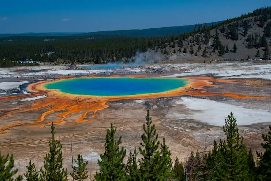 A breathtaking view of the Grand Prismatic Spring in Yellowstone National Park, with its vibrant blue, green, and orange hues, surrounded by the rugged landscape of the park, showcasing the awe-inspiring beauty and geological wonders that await travelers in America's national parks and natural treasures along the coast-to-coast route.